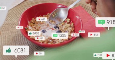 Mutfak masasında mısır gevreği kepçeleyen yeşil tişörtlü bir adam yüzen dijital pazarlama ikonları gösteriyor. Kahvaltı, sağlıklı, modern, kentsel, sağlık, gurme, canlı