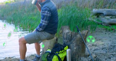 Göl kenarındaki bardaktan yudumlayan bir adam yüzen yeşil AR yenilenebilir enerji ikonları gösteriyor. Doğa, macera, sürdürülebilirlik, açık hava, sükunet, çevre dostu, keşif