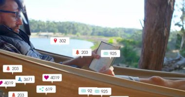 Göl kenarındaki hamakta uzanan adam kitap okuyor, sosyal medya animasyon ikonları sergiliyor. Rahatlama, rahatlama, doğa, dinginlik, dijital etkileşim, açık hava inzivası, refah