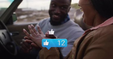 Arabanın içinde yüzüklerini değiş tokuş eden çift, yüzen başparmak simgeleri ve sosyal medya baloncukları gösteriyor. Romantizm, bağlılık, kutlama, aşk, dijital, bağlantı, yakınlık