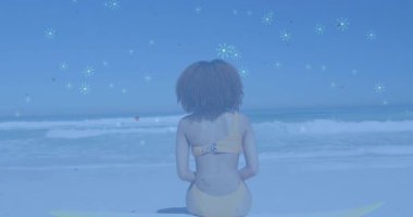 Sahil şeridinde sörf tahtasında oturan kadın kalp ikonlarıyla kaplanmış sağlık analizleri sergiliyor. Tatil, macera, eğlence, coşku, refah, yaşam tarzı, doğa