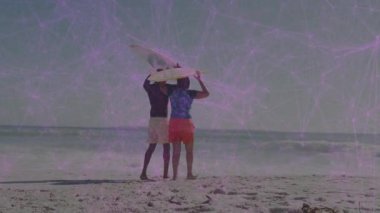 Güneşli sahilde sörf tahtası kaldıran bir çift, mor ağ çizgileriyle donatılmış bir teknoloji sergiliyor. Macera, bağlantı, dinginlik, sahil, canlılık, uyum, rahatlama