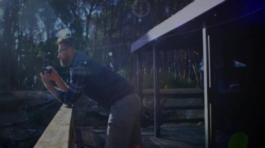 Verandaya yaslanan bir adam doğa fotoğrafçılığı için ormanın güneş ışığını dijital kamerayla yakalıyor. Doğa, keşif, açık hava, dinginlik, macera, köy keşfi