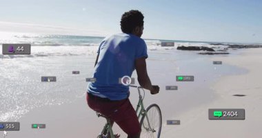 Sahilde bisiklet süren bir adam, dijital pazarlama için yüzen sosyal medya simgeleri sergiliyor. Spor, eğlence, açık hava, eğlence, teknoloji, bağlantı, macera.