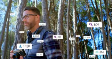 Erkek fotoğrafçı ormanın içinde kamera tutuyor, yüzen sosyal medya pazarlama ölçümleri gösteriyor. Doğa, kaşif, manzara, açık hava, dijital, analitik, macera