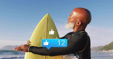 Olgun bir adam güneşli plajda sörf tahtası tutuyor, sosyal medya ölçümlerini baş parmağıyla gösteriyor. Macera, canlılık, rahatlama, açık hava, fitness, kıyı, dinamik