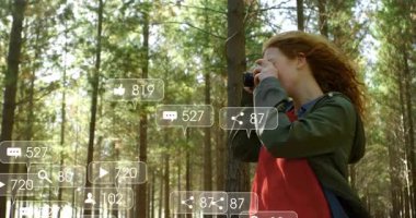 Kadın fotoğrafçı çam ormanında kamera kaldırıyor, yüzen sosyal medya pazarlama ikonları sergiliyor. Doğa, açık hava, macera, teknoloji, iletişim, keşif, huzur