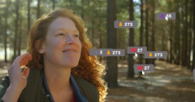 Çam ormanlarında yukarı bakan bir kadın, yüzen sosyal medya pazarlama nişan ikonları sergiliyor. Doğa, açık hava, canlı, dijital, bağlantı, dinginlik, yaşam tarzı