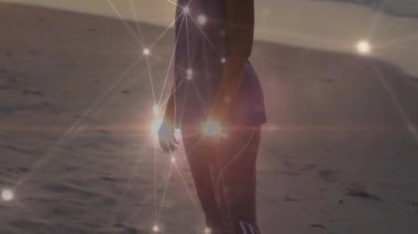 Alacakaranlıkta kumsalda yürüyen bir kadın parlayan ağ düğümleriyle teknoloji bağlantısı sergiliyor. Gelecek, bağlantı, sükunet, siluet, teknoloji, dinginlik, dijital
