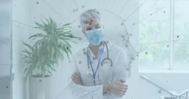 Kıdemli doktor maske ve steteskop takıp klinik koridorunda yürüyor ve yüz tanıma işaretleri gösteriyor. Sağlık, sağlık, profesyonellik, teşhis, hastane, sağlık, teknoloji