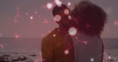 Sakallı bir adam sahilde kıvırcık saçlı bir kadını kucaklıyor. Teknoloji için kırmızı ağ örtüsü gösteriyor. Romantik, bağlantı, iletişim, teknoloji, fütürist, samimi, aşk