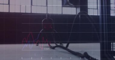 Endüstriyel jimnastik salonunda savaş halatları sallayan finans sektörü için finans hattı grafikleri hazırlayan bir adam. Fitness, strength, training, industrial, modern, dynamic, performance