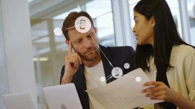 Teknoloji ofisinde, olgun erkek ve kadın kağıtları inceliyor, telefon müzik ikonları ile ağ örtüyor. İşbirliği, fütürizm, yenilik, dijital bağlantı, profesyonel, işyeri, takım çalışması