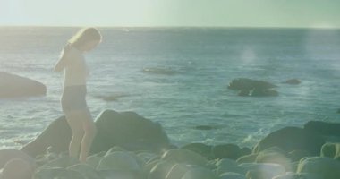 Kayalık sahilde yalınayak yürüyen bir kadın, yüzen sağlık ikonu ve kalp atış hızı grafiği ile. Sahil, huzur, doğal, açık hava, huzur, macera, sağlık.