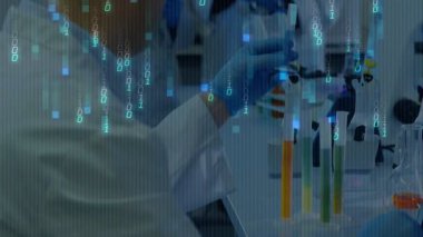 Laboratuvardaki bilim adamları güvenlik gözlüğü takıp hunideki pipetle ilgileniyorlar ve ikili kod akışları gösteriyorlar. Araştırma, yenilik, teknoloji, kesinlik, deney, bilimsel, analiz