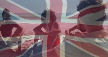 Beş arkadaş güneşli sahilde oturmuş gülüyor, Union Jack bayrağını örtüyor seyahat pazarlaması yapıyor. Plaj, rahatlama, tatil, boş zaman, açık hava, arkadaşlık, coşku