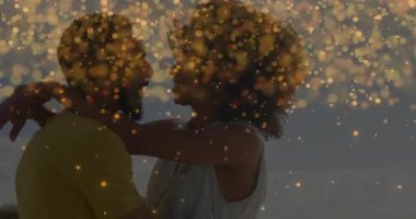 Alacakaranlıkta kumsalda bir adama sarılan kadın, pazarlama için romantizmi kutlayan altın bokeh parçacıklarıyla. Romantizm, samimiyet, kutlama, sıcaklık, dinginlik, hayal gücü, bağlantı