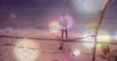 Kıyı şeridinde duran adam, yüzen pastel bokeh sağlık simgeleriyle okyanusa bakıyor. Kıyı, sükunet, meditasyon, sağIık, dinginlik, tefekkür, doğa