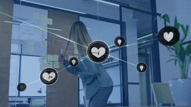 Kadın pazarlama ofisinde camlara yapışkan notlar düzenliyor, yüzen kalp ve ampul simgeleriyle. İşbirliği, beyin fırtınası, yenilik, üretkenlik, modernlik, dijital, işyeri