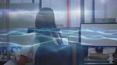 İş yerinde masa başında çalışan, bilgisayar ekranlarından dalga boylarını gösteren bir bayan çalışan. Teknoloji, işbirliği, yenilik, üretkenlik, modernlik, çalışma alanı, iletişim