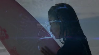Sörf tahtası tutan bir kadın kıyıda duruyor, mavi holografik arayüzlü bir teknoloji sergiliyor. Teknoloji, dijital, fütüristik, yenilik, macera, açık hava, minimalist