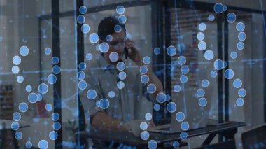 Gözlüklü bir adam, mavi ağ grafiklerini göstererek, teknoloji masasında aynı anda birden fazla iş yapıyor. Teknoloji, bağlantı, modern, profesyonel, yenilik, çalışma alanı, dijital