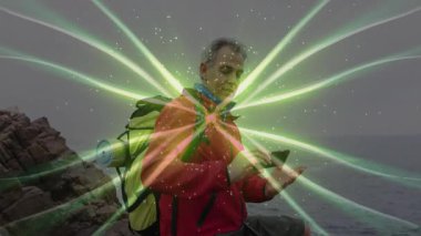 Kayalık sahilde akıllı telefon tutan, yeşil dijital ışınlar yansıtan, teknoloji konseptini sergileyen bir adam. Macera, teknoloji, yenilik, açık hava, keşif, bağlantı, doğa