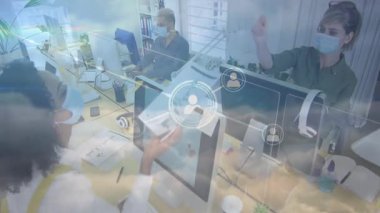 Maskeli iş arkadaşları açık-plan iş ofisindeki masaüstü monitörlerinde yazarak ağ örtüşmelerini gösteriyorlar. İşbirliği, çalışma alanı, teknoloji, bağlantı, profesyonellik, modern, takım