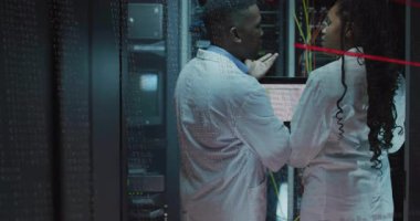 İki bilişim teknisyeni veri merkezinde sunucu raflarını inceliyor, yüzen kod ve yanıp sönen ışıklarla. Teknoloji, siber güvenlik, yenilik, dijital, altyapı, profesyonellik, modern