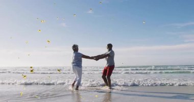 Erkek ve kadın kumlu sahilde hafif dalgalarla dans ediyor, sağlık ölçümleri gösteren animasyon kalp ikonu. Romantik, ahenkli, boş, kıyı manzaralı, zamansız, sağlıklı.