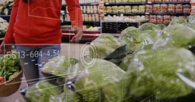 Elinde yeşillikler olan ve perakende reyonunda lahanalara uzanan dişi alışverişçi, yüzen veri panellerini gösteriyor. Taze ürün, sağlıklı beslenme, dijital perakende, market alışverişi, modern ticaret, refah, tüketici davranışı