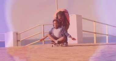 Deniz kenarındaki gezinti alanında kaykaylı çocuğa rehberlik eden ebeveyn animasyon teknolojisi veri tablolarını gösteriyor. Macera, açık hava aktivitesi, güvenlik, aile, eğlence, sahil, gençlik