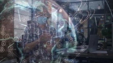 Yüz maskesi takan bir adam teknoloji ofisinde dizüstü bilgisayarda çalışıyor, dönen dünya ve ağ simgeleri gösteriyor. İşbirliği, teknoloji, veri görselleştirme, ağ, işyeri, yenilik, modern