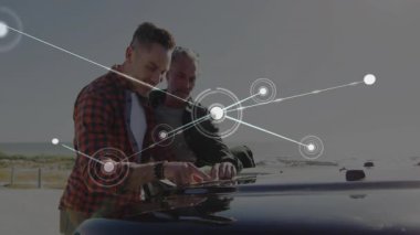 Sahil gözcülüğünde araba kaputuna yaslanan iki adam, teknoloji ağı grafiğini parlayan düğümlerle örtüyor. Teknoloji, bağlantı, yenilik, işbirliği, açık hava, eğlence, modern