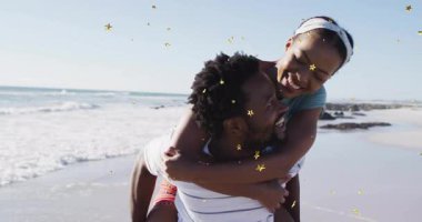 Adam kumsaldaki kadını sırtında taşıyor, seyahat pazarında altın yıldızlı konfeti sunuyor. Romantizm, eğlence, rahatlama, mutluluk, kutlama, açık hava, canlı