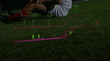 Erkek futbolcu geceleri çim sahada dizini sıkıca tutarak spor analizinin dijital grafiklerini gösteriyor. Sporcu, spor, yarışma, fütüristik, dijital, açık hava, sakatlık