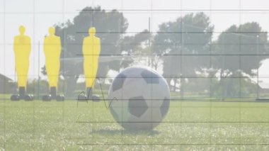 Futbol oyuncusu spor teknolojisi eğitiminde mankenlerin yanında topu kontrol ediyor, veri örtülerini gösteriyor. Atletizm, takım çalışması, hassasiyet, rekabet, açık hava, fitness, strateji