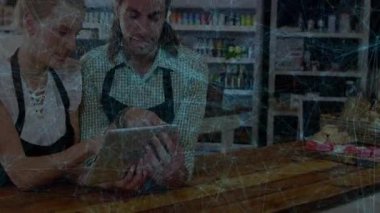 Perakende mağazası asistanları ahşap tezgahın arkasında tablet kullanarak satış verilerini yüzen grafiklerle takip ediyorlar. Perakende, işbirliği, teknoloji, kafe, içişleri, verimlilik, profesyonellik