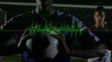 Futbolcular gece kalenin önünde durmuş, spor teknolojisi dalga boyu örtüsünü vurguluyorlar. Sporcular, yarışma, yenilik, dijital, gece manzarası, hareket, spor