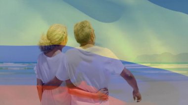 Kıdemli çift kumsalda kucaklaşıyorlar, seyahat reklamı için hareketli dalgalarla bayrak kaplıyorlar. Romantizm, sükunet, tatil, dinginlik, arkadaşlık, uyum, doğal