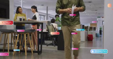 Dizüstü bilgisayarı inceleyen iki kadın, iş yerinde belgelerle yürüyen bir adam, yüzen veri etiketleri gösteriyor. İşbirliği, takım çalışması, modernite, veri analizi, profesyonel, üretkenlik, teknoloji