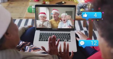 Büyükanne el sallıyor, kızı kanepede el sallıyor, dizüstü bilgisayarın etrafında hediye ikonu gösteriyor. Aile, teknoloji, kutlama, konfor, sıcaklık, bağlantı, gelenek