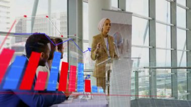 Cam duvarların içinde podyumda sunulan türbanlı kadın, animasyon finans çizelgeleri gösteriyor. Kurumsal, profesyonellik, modernlik, başarı, çeşitlilik, iletişim, strateji