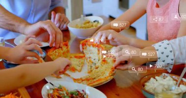 Aile yemek masasında pizza dilimleri alıyor, sosyal medya animasyonlarıyla örtüşüyor. Mutfak, birliktelik, sıradan, kırsal, mutlu, yaşam tarzı, nişan