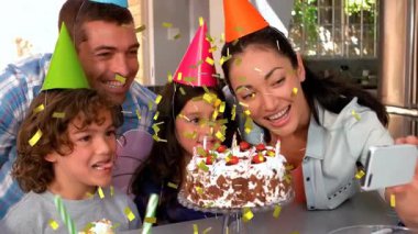 Modern mutfakta selfie çeken aile, doğum günü pastası etrafında altın konfeti gösteren teknik animasyon. Kutlama, birliktelik, neşe, mutluluk, evcil, modern, yaşam tarzı