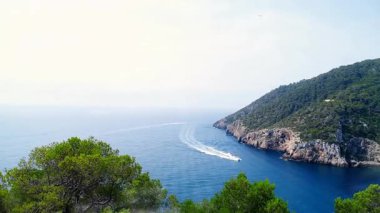 Beyaz motorlu tekne kıvrımlı bir şekilde denizi geçerek kayalık kayalıkları ve çam ağaçlarının tepelerini 3 boyutlu olarak çiziyor. Deniz manzarası, macera, minimalizm, seyahat, açık hava, doğa, huzur