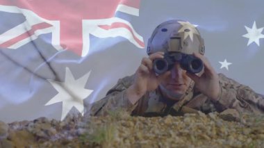 Erkek asker çakıl yığını üzerinde yatarken açık Avustralya bayrağını askeri kullanım için üstüste koyuyor. Ordu, keşif, kamuflaj, arazi, açık hava, strateji, gözetim.