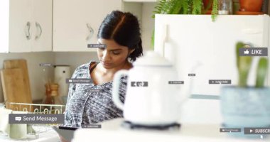 Kadın, evdeki mutfakta tabletle etkileşime giriyor, yüzen sosyal medya etiketleri sergiliyor. Teknoloji, yaşam tarzı, minimalizm, ev halkı, iletişim, modern, samimi