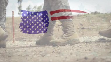 İki asker, kamuflaj pantolonu ve taktik botlarıyla çakıl taşları üzerinde yürüyor, stilize Amerikan bayrağını örterek. Ordu, vatanseverlik, sert, açık hava, disiplin, cesaret, üniforma.