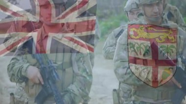 Ormanda dikilen altı erkek asker, İngiliz bayrağı ve Fiji arması ile savunma verilerini gösteriyorlar. Ordu, savunma, kamuflaj, taktik, takım çalışması, orman, keşif